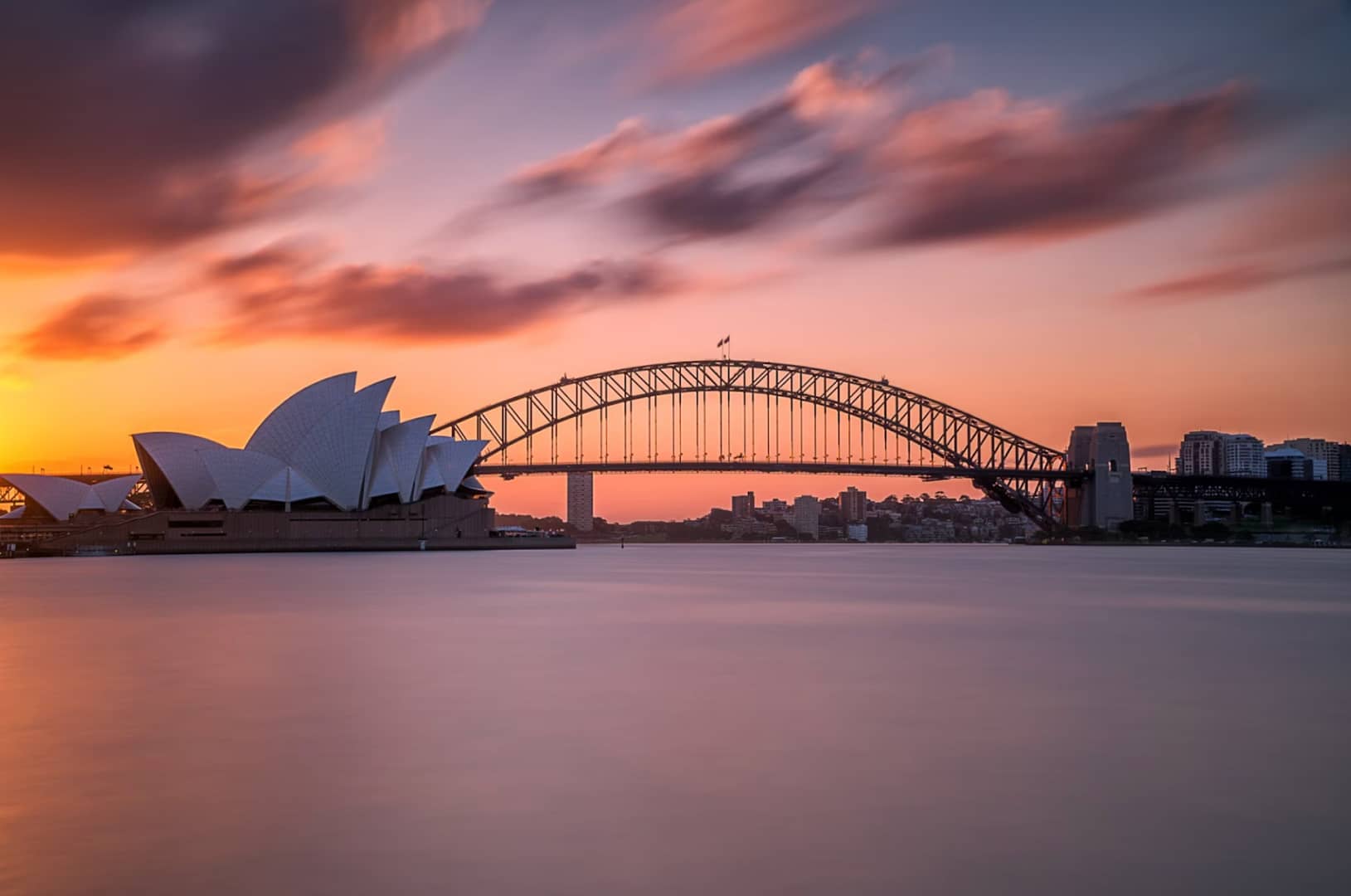 Mid ground shot of the sydney harbor bridge with a light pink and blue sky